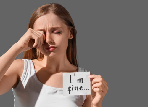 Photo of a crying woman holding up a post-note that says 